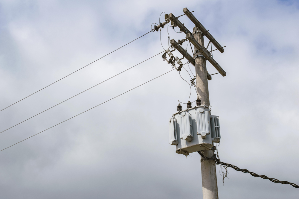 Electricity transformer mounted on a utility pole with overhead power lines against a cloudy sky.